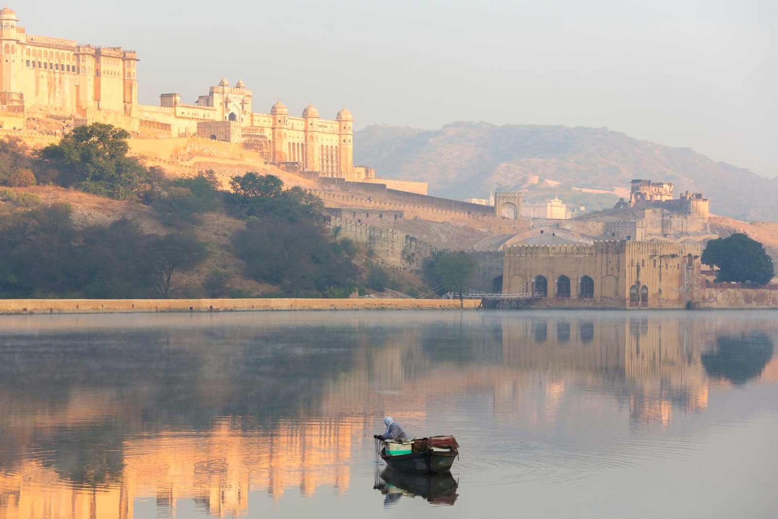 Jaipur,India,Fisherman in boat on calm lake at sunrise, large fort on hill in the distance.