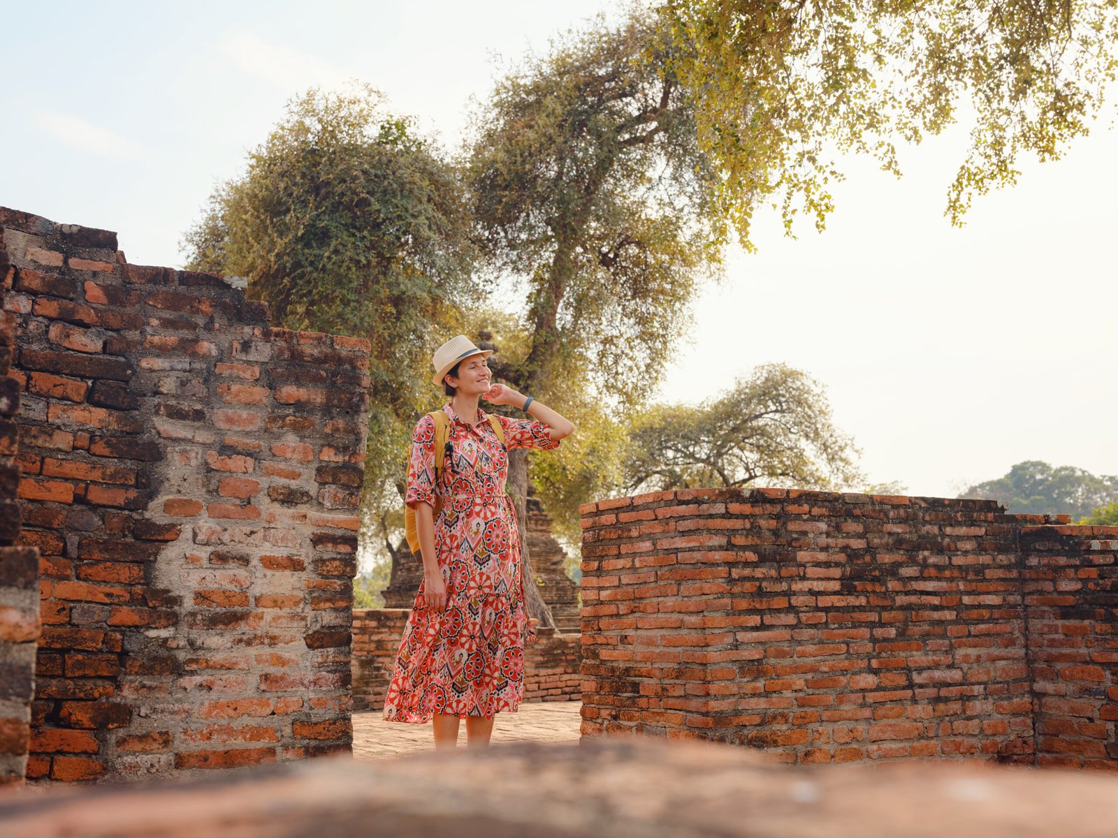 Young female tourist in dress exploring historic park of Ayutthaya, Thailand. Surrounded by ancient temples and statues, she enjoys peaceful atmosphere and rich cultural heritage.